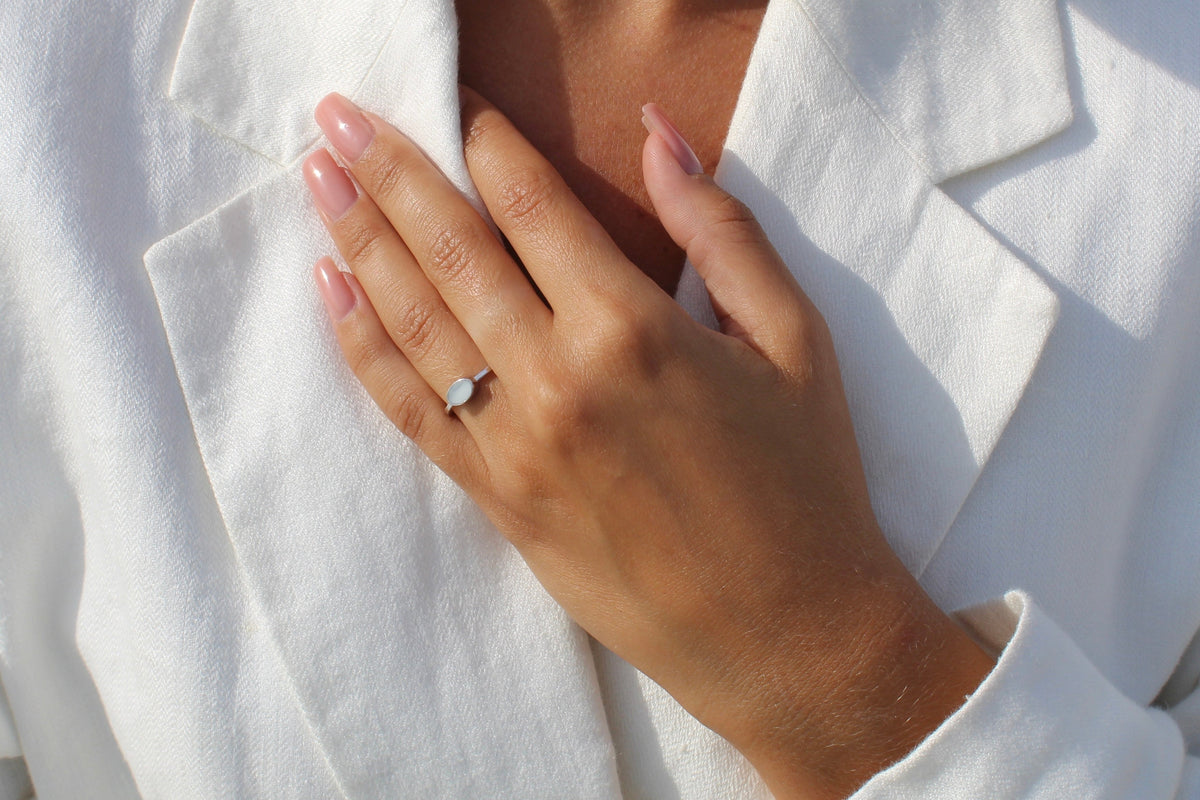Hand flat on a white linen jacket, wearing the silver-toned Juna ring with a sideways oval milk stone