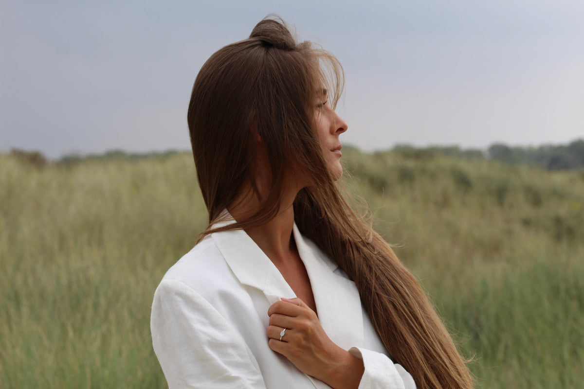 Woman in a white blazer in the dunes, hand at her collar wearing the silver Juna breast milk ring