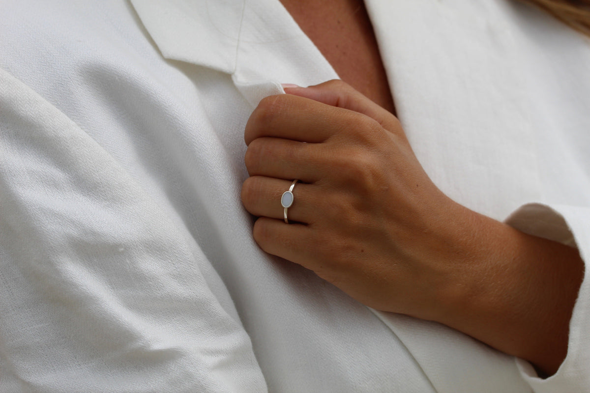 Hand holding a white linen lapel, wearing the silver Juna ring with a horizontal oval milk stone
