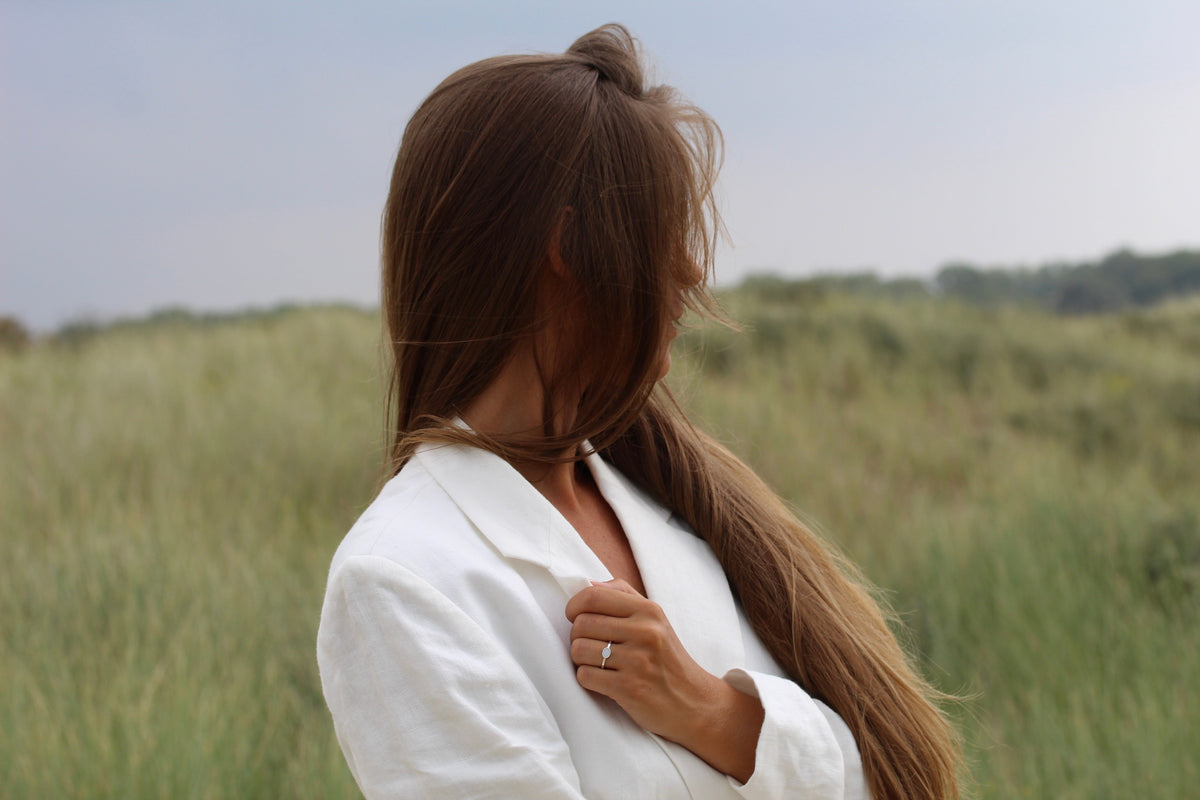 Woman with hair over her face in the dunes, wearing the silver-toned Juna breast milk ring
