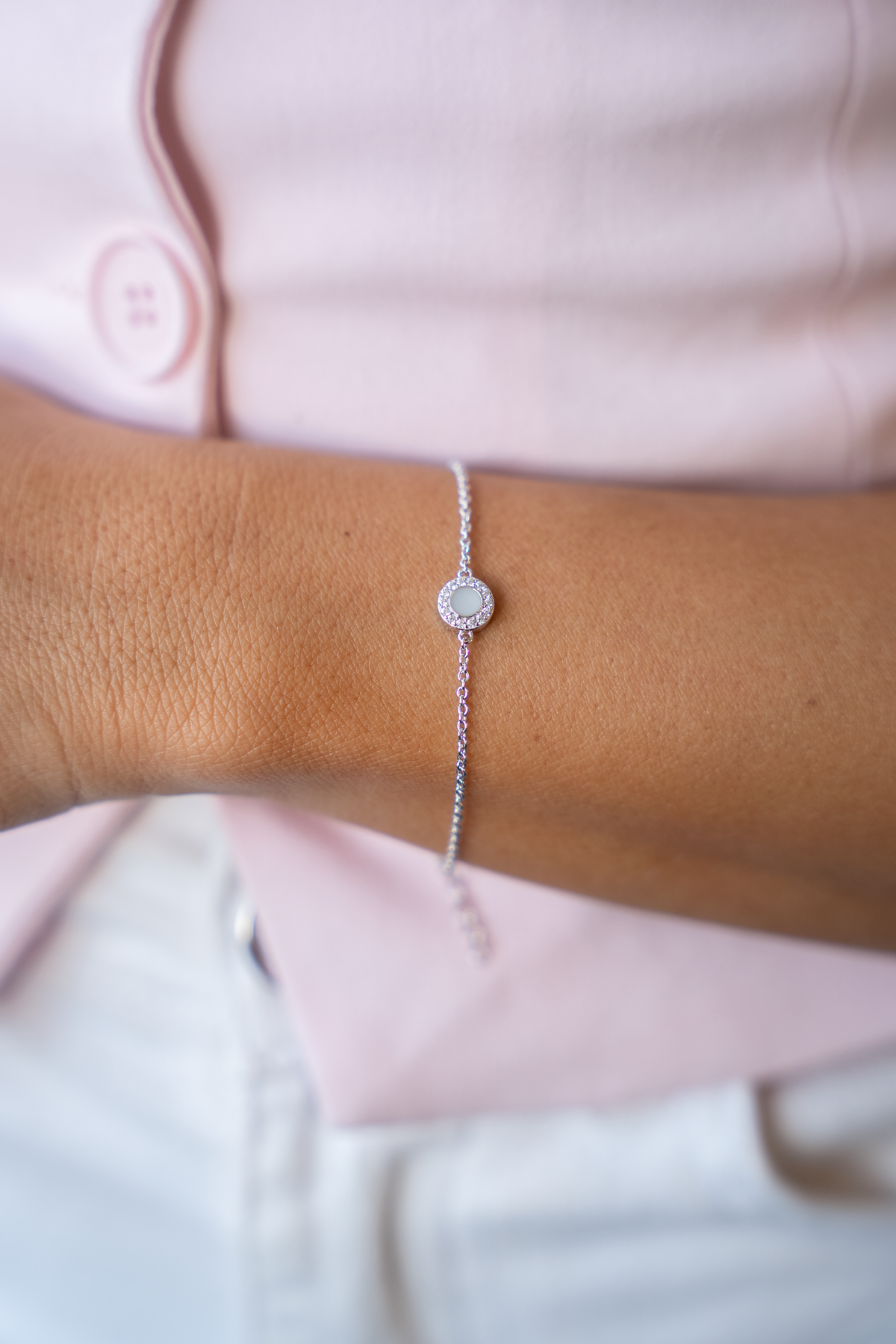 Silver Juul breast milk bracelet with halo-set round milk stone worn on a wrist, pink blazer behind
