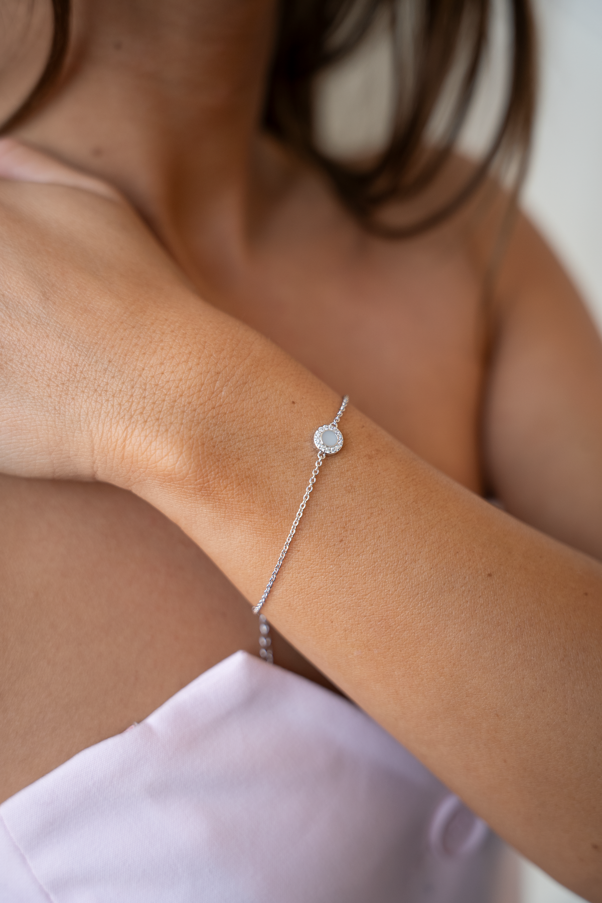 Silver Juul breast milk bracelet with round halo milk stone on a woman's wrist across her chest