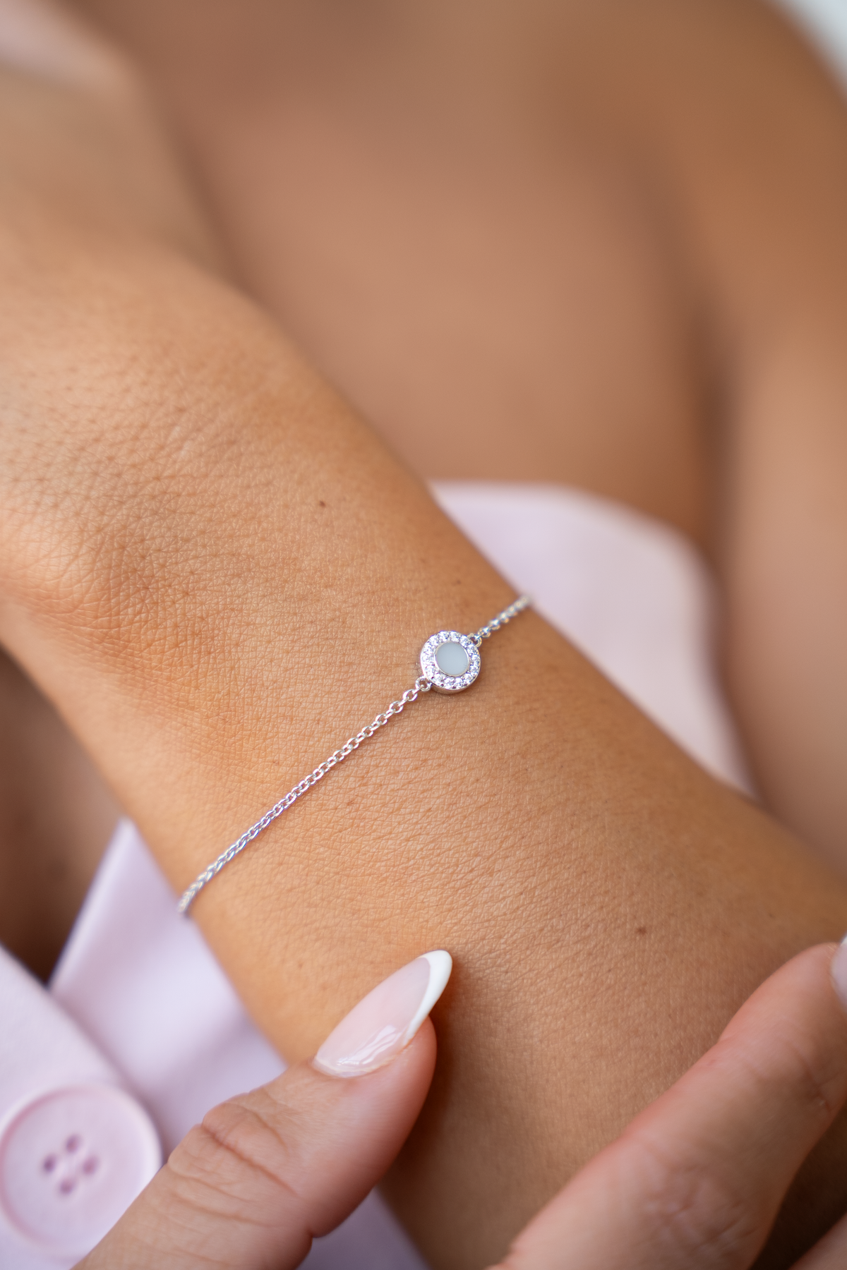 Close-up of a silver Juul breast milk bracelet with round milk stone and halo of clear stones on a forearm