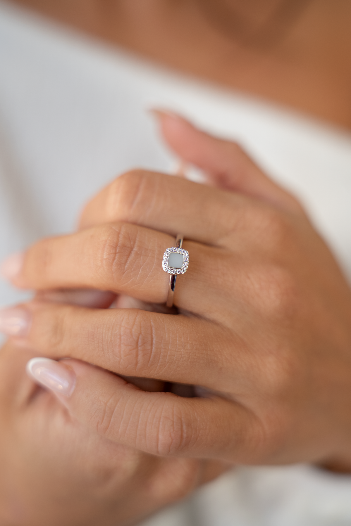 Close-up of a hand wearing the silver-toned Lara ring with a cushion-shaped milk stone and stone halo