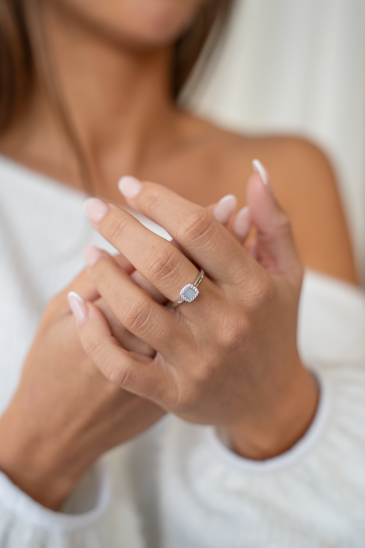 Hands clasped in front of a white sweater, wearing the silver-toned Lara breast milk halo ring