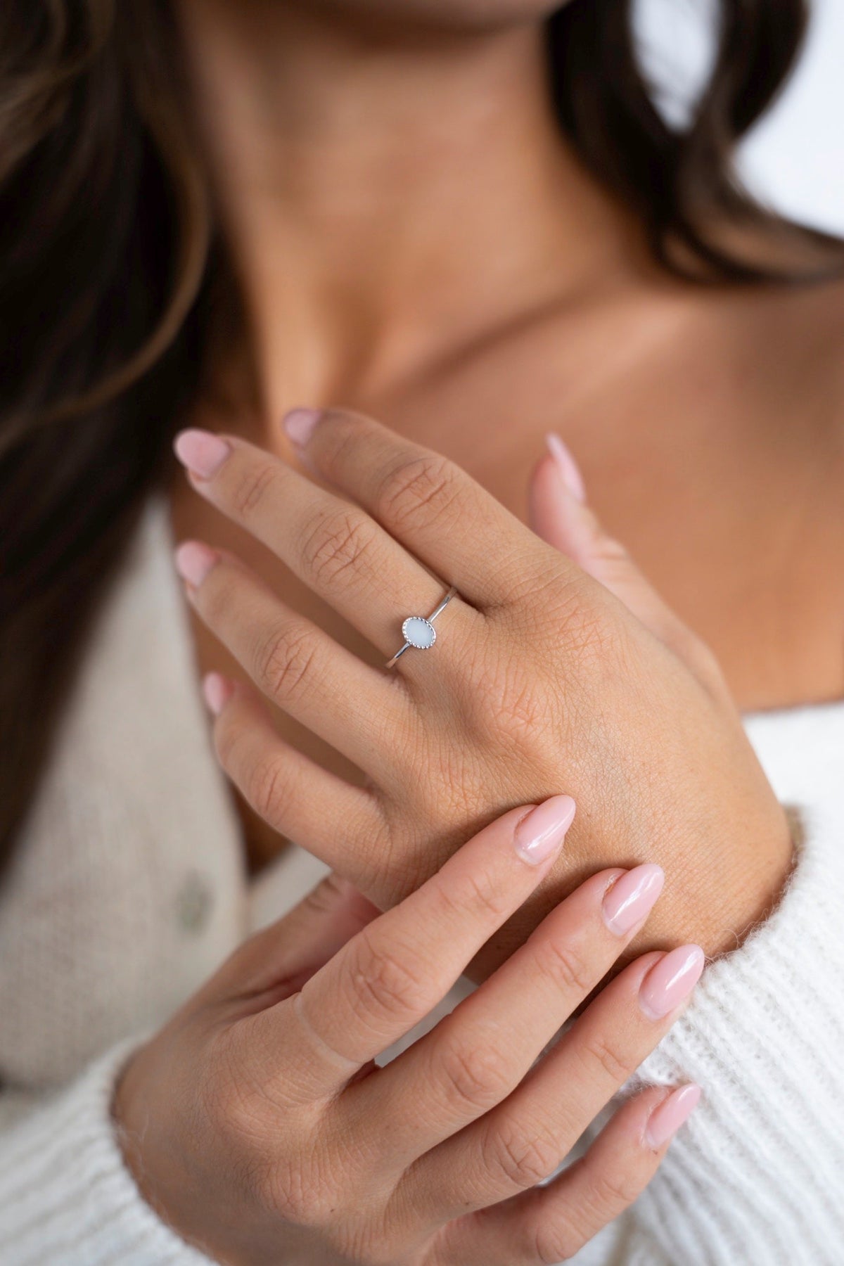 Hands crossed in front of a white sweater, wearing the Lauren breast milk ring in silver on the ring finger.