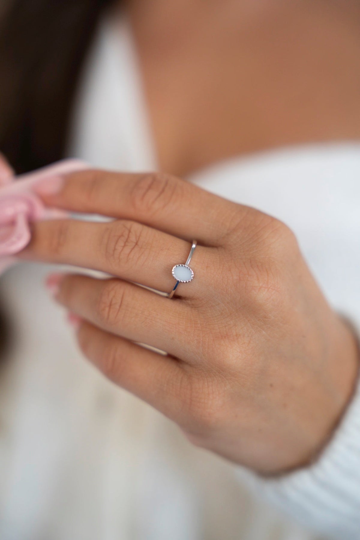 Close-up of the Lauren ring in 925 sterling silver with an oval breast milk stone, the hand holding a pink pacifier.