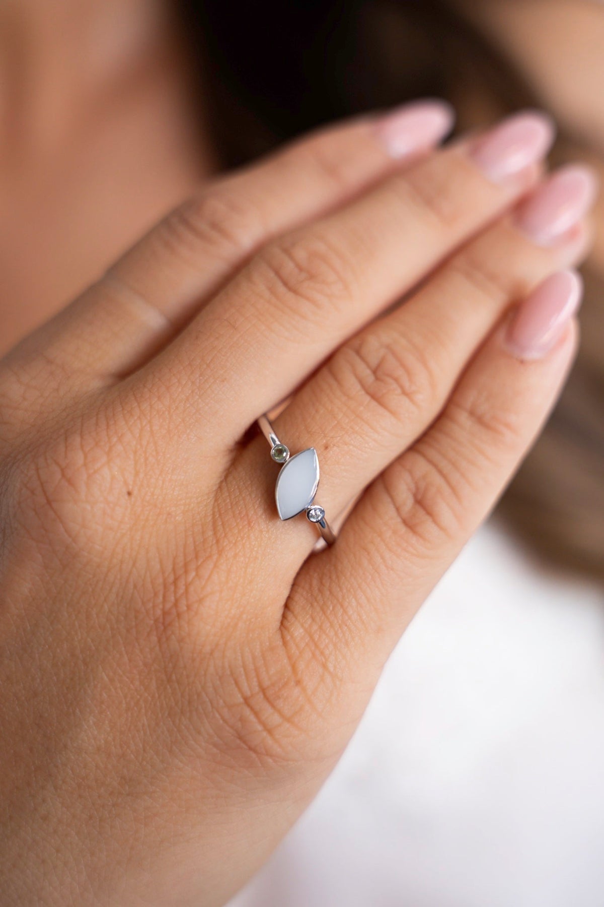 Close-up of the silver Lina Duo ring: an oval breast milk stone between two small birthstones, worn on the hand.