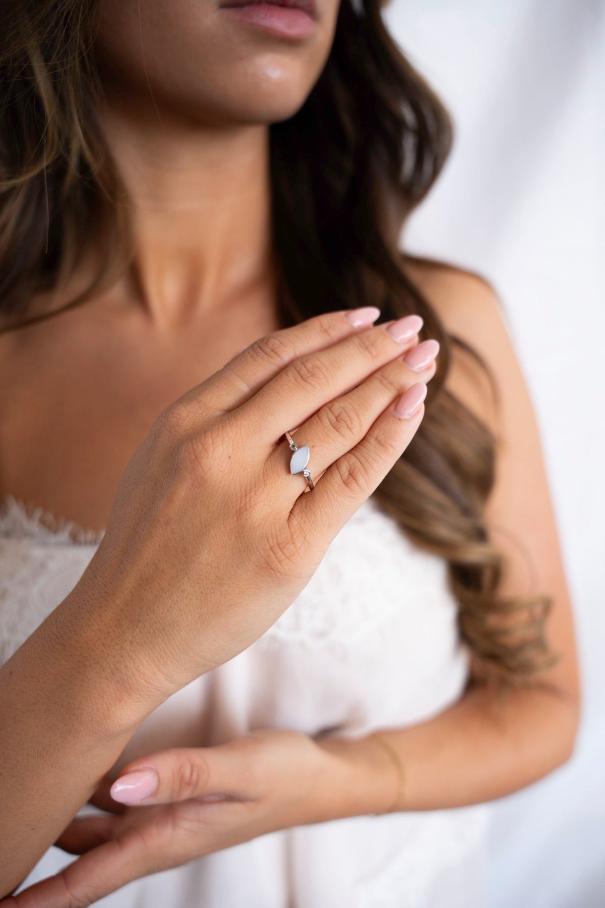 Woman in a white lace top wearing the Lina Duo breast milk ring in solid white gold on her ring finger.