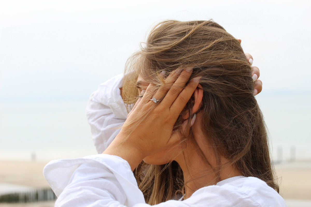 Lina ring in white gold on the finger, woman on the beach with her hand in windblown hair