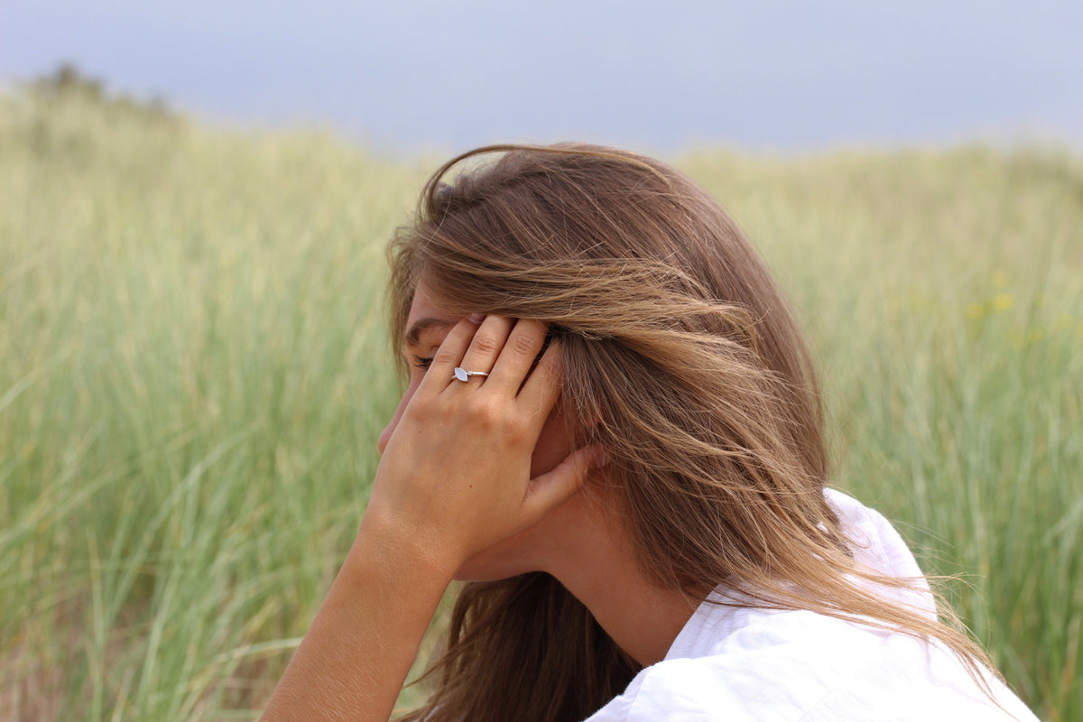 Lina ring in white gold on the finger, woman in dune grass resting her hand against her head
