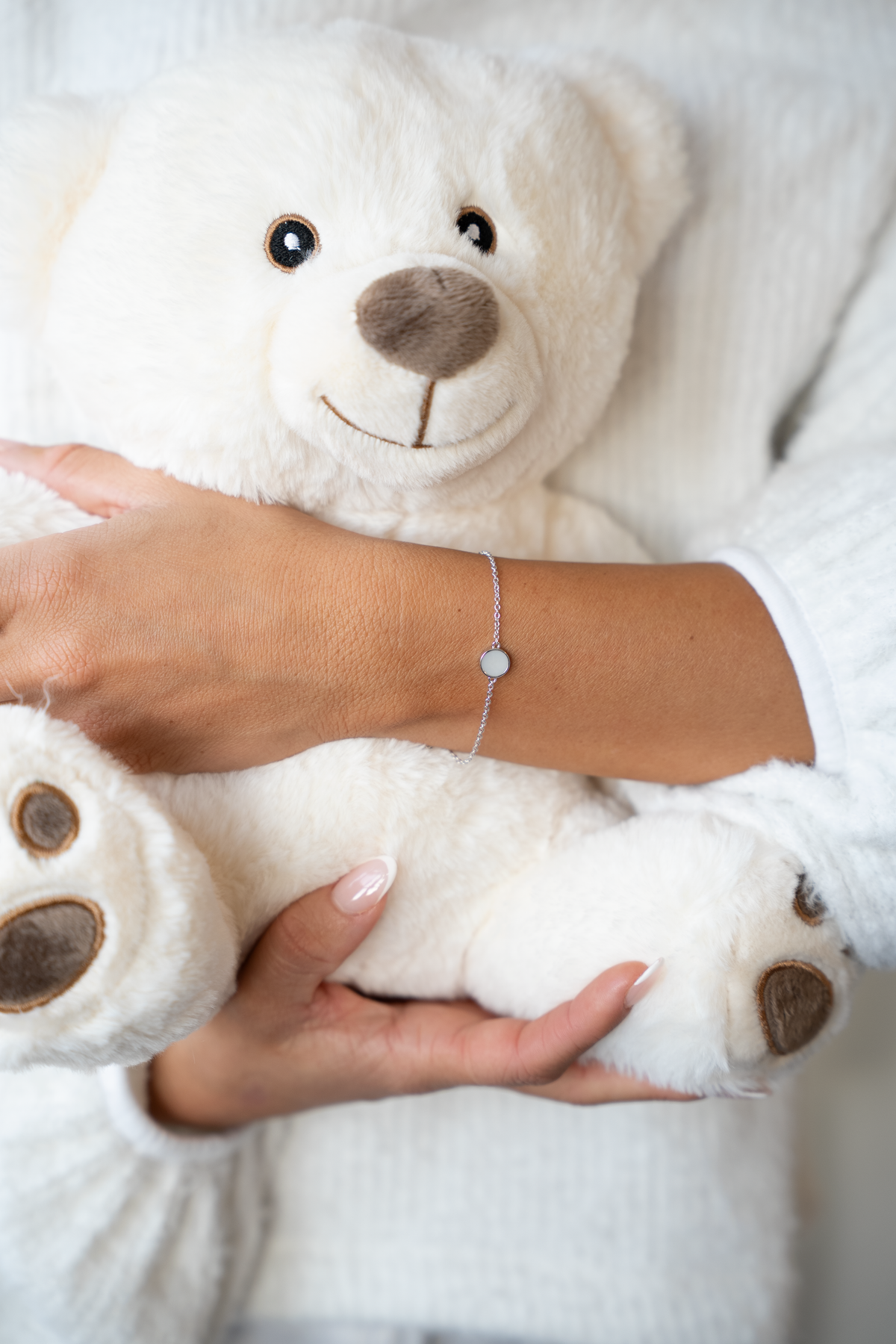 Woman holding a white teddy bear, wearing the silver Lis breast milk bracelet with round milk stone