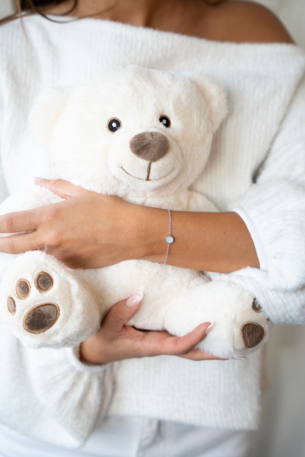 Woman in a white sweater hugging a teddy bear, wearing the silver Lis breast milk bracelet