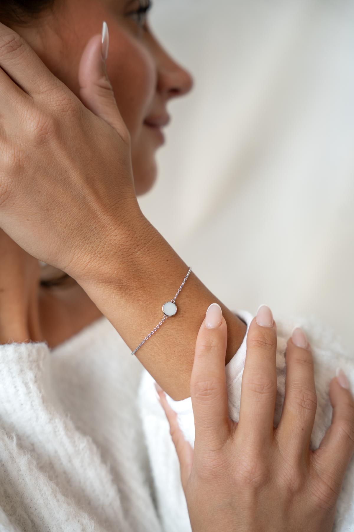 Woman in profile with her hand at her ear, wearing the silver Lis breast milk bracelet