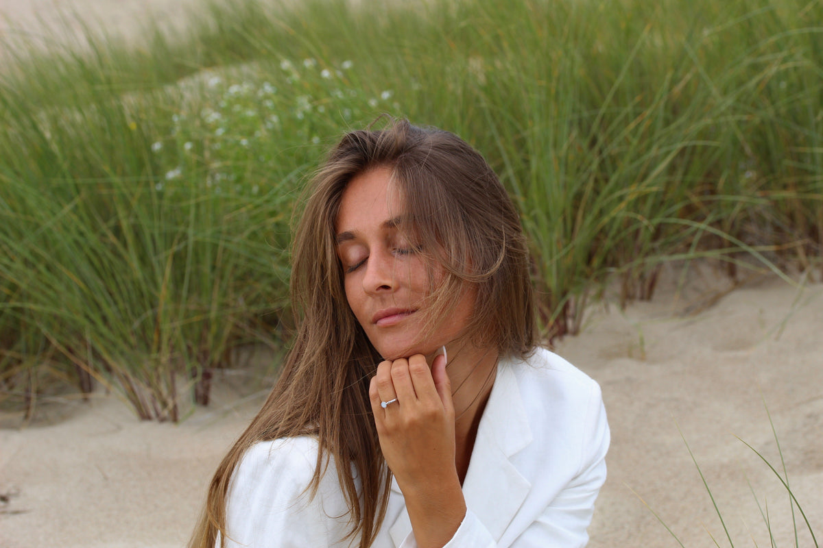 Silver Lis ring on the finger, woman in a white blazer resting her chin on her hand