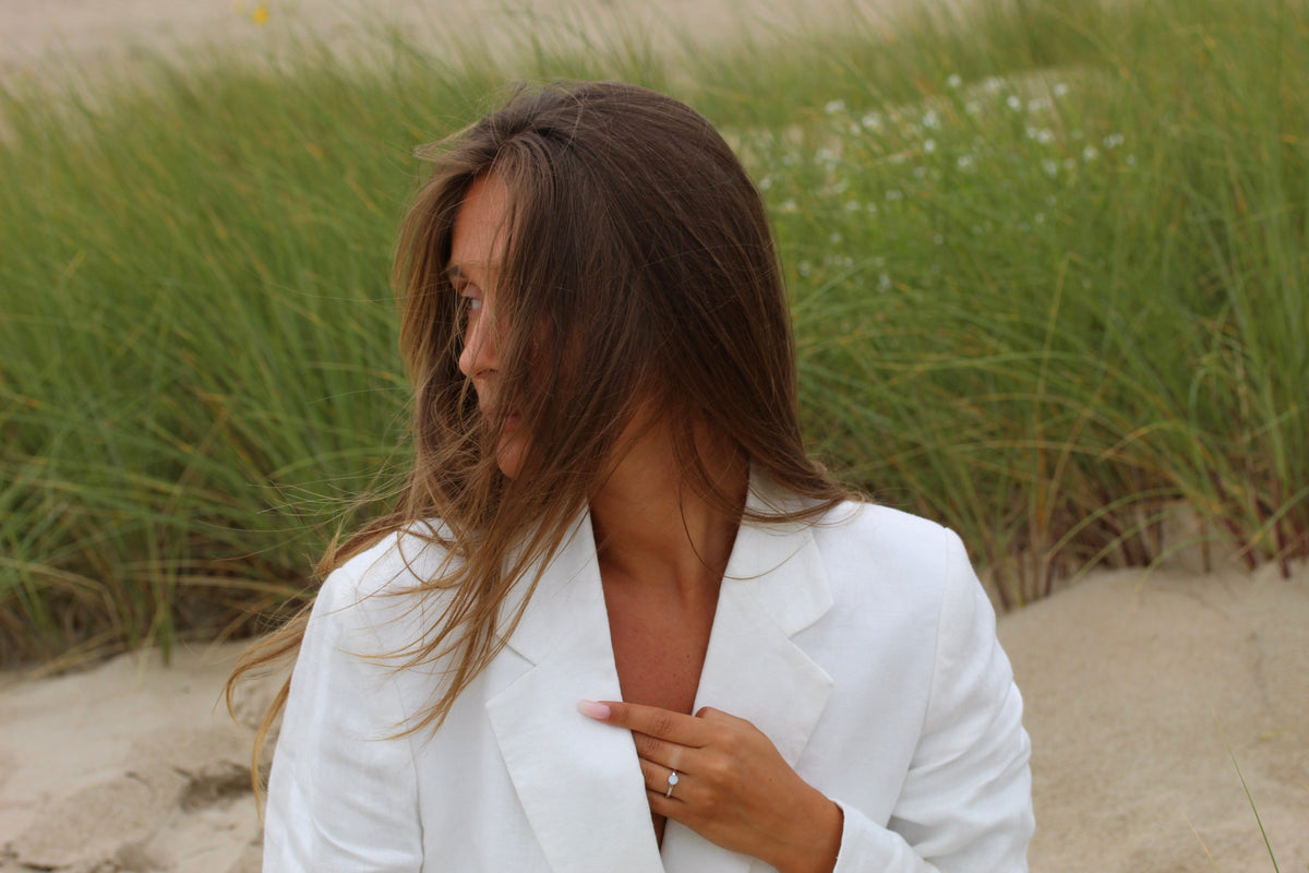 Silver Lis ring on the finger, woman in a white blazer in the dunes