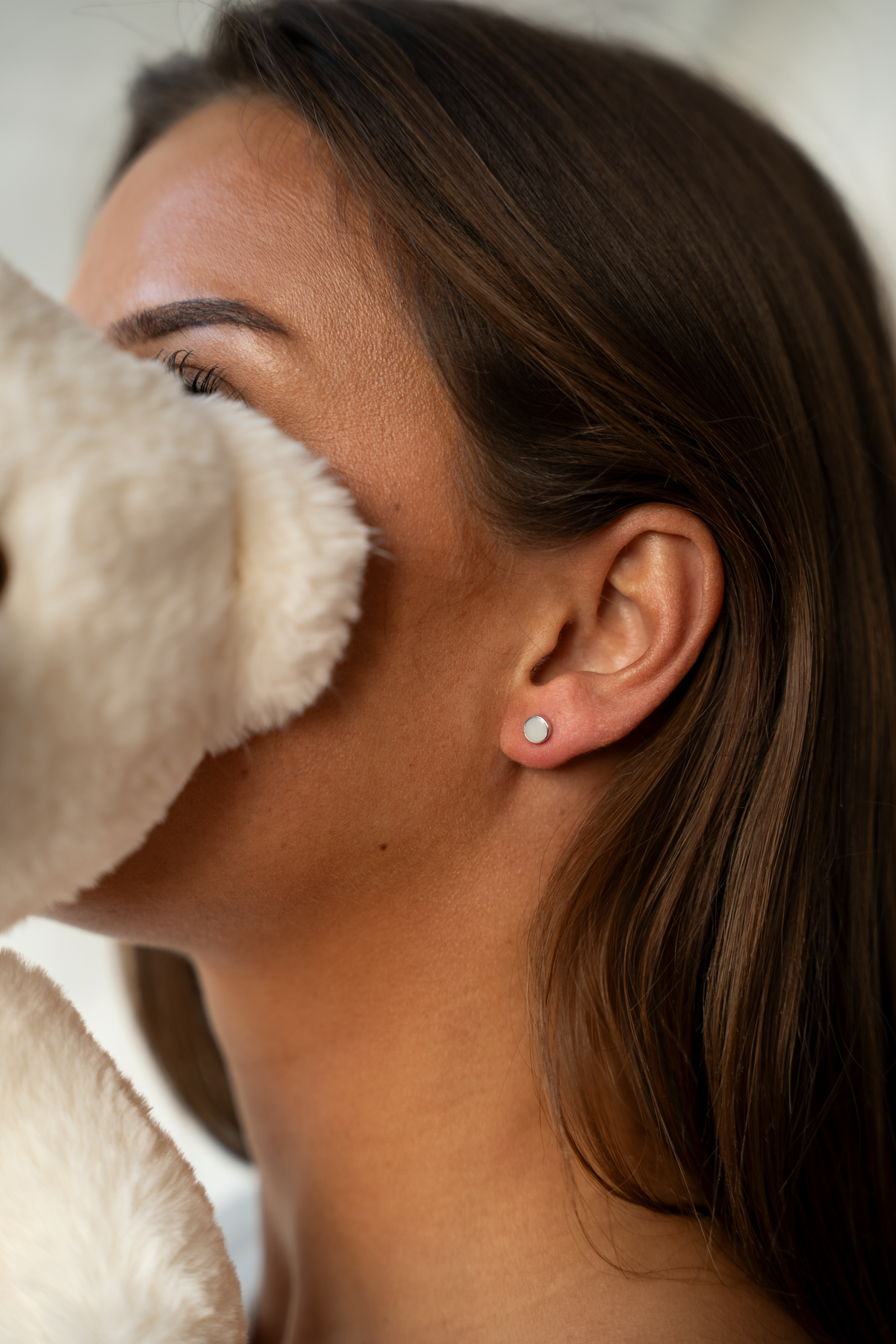 Woman partly hidden by a plush teddy bear, wearing one Lis silver round breast milk stud