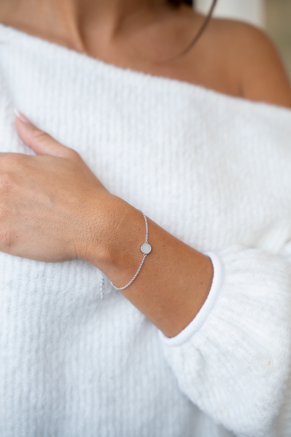 Silver Lis breast milk bracelet with round milk stone worn on a wrist against a white knit sweater