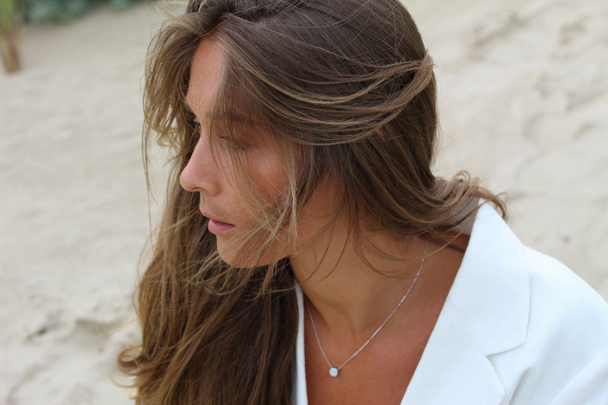 Woman with windswept hair on the beach wearing a silver-colored Lis round breast milk necklace