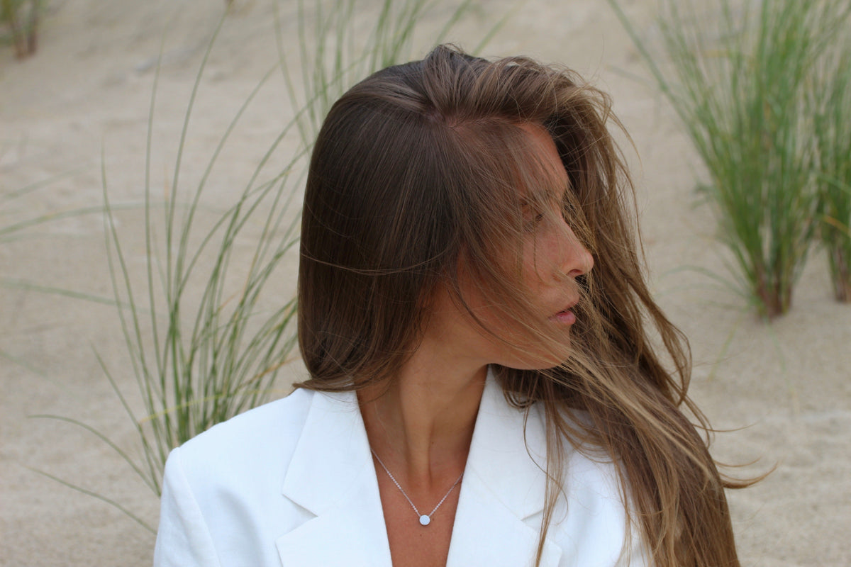 Woman in a white blazer in the dunes, small round Lis breast milk pendant at her neckline