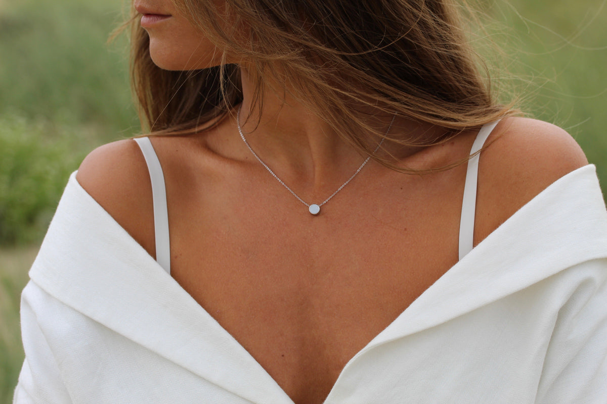 Lis round breast milk necklace on the collarbone of a woman in an off-shoulder white top