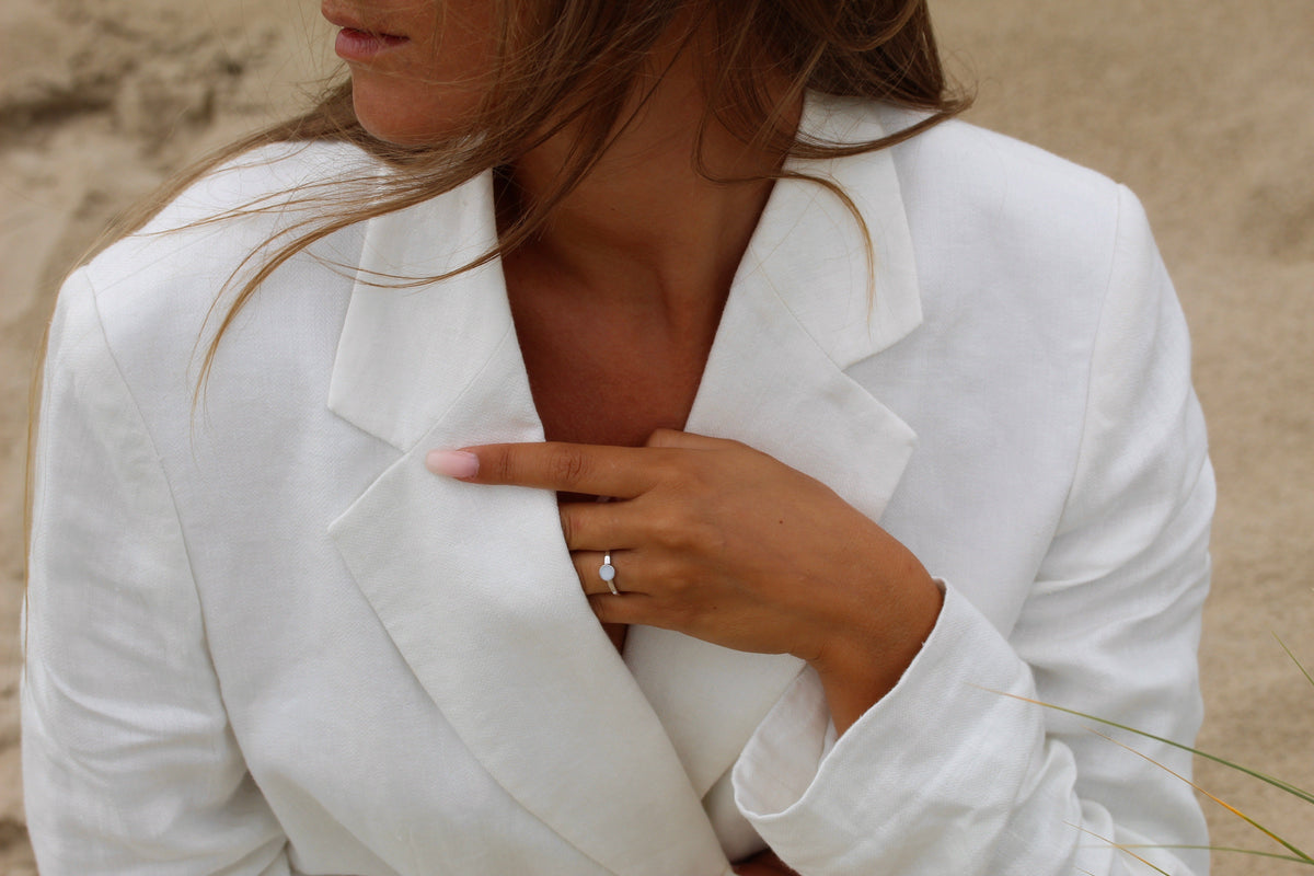 Lis ring in white gold on the finger, close-up of a hand on the lapel of a white blazer