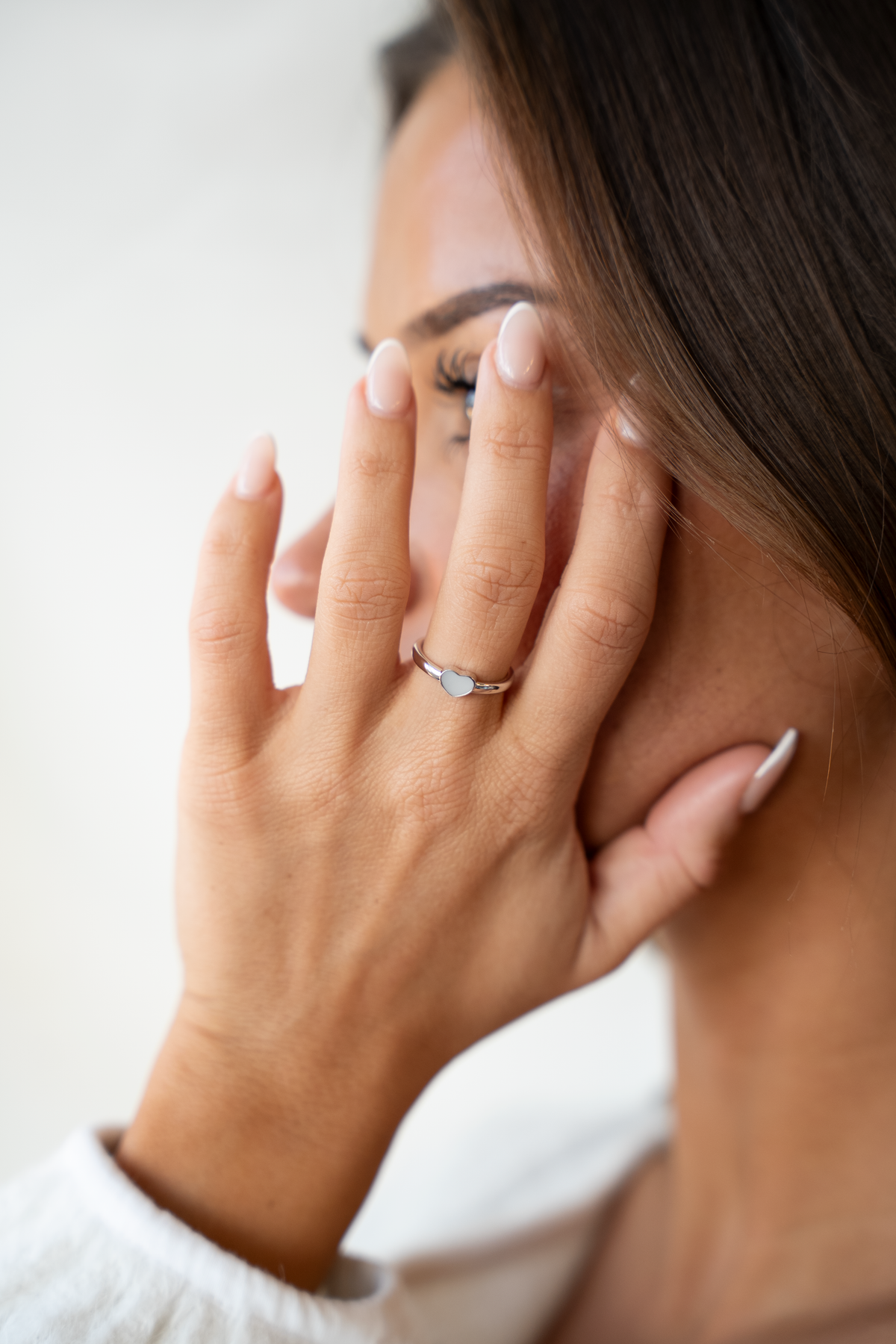 Lisa heart ring in white gold on the finger, hand resting against the cheek, close-up