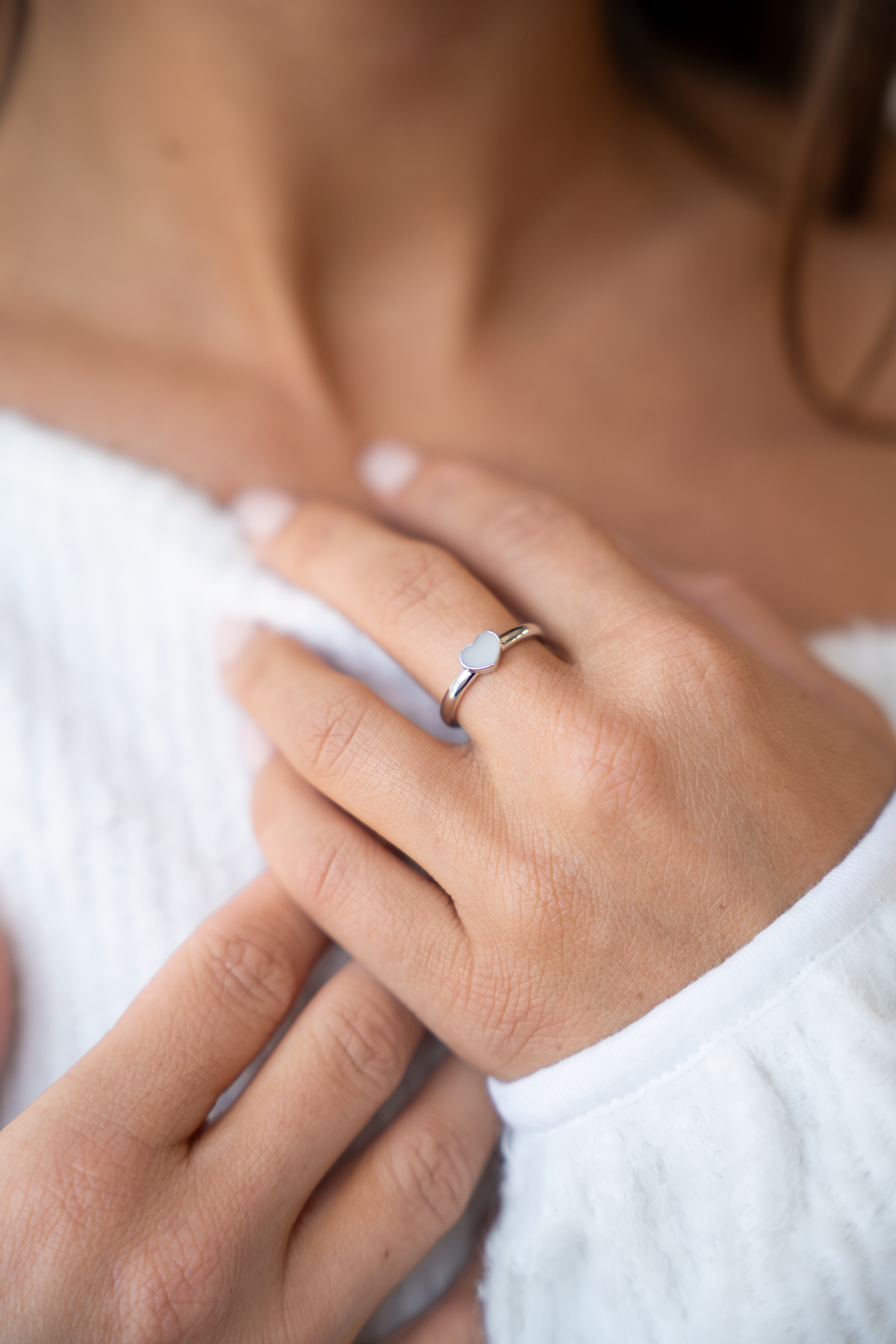 Lisa heart ring in white gold on the finger, hand at the neckline of a white knit sweater