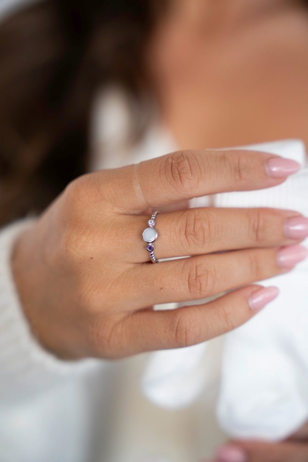 Lot ring in silver with a round breast milk stone between two birthstones, worn in front of a white sweater.