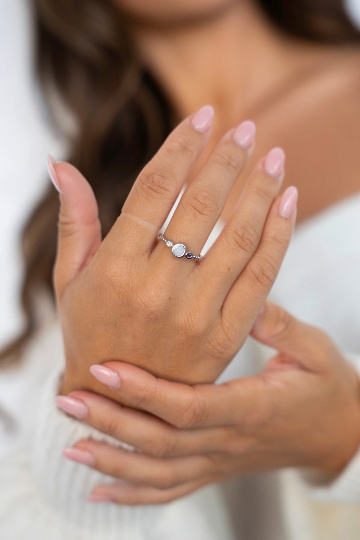 Lot breast milk ring in solid white gold with three stones in a row, on a hand resting on the other hand.