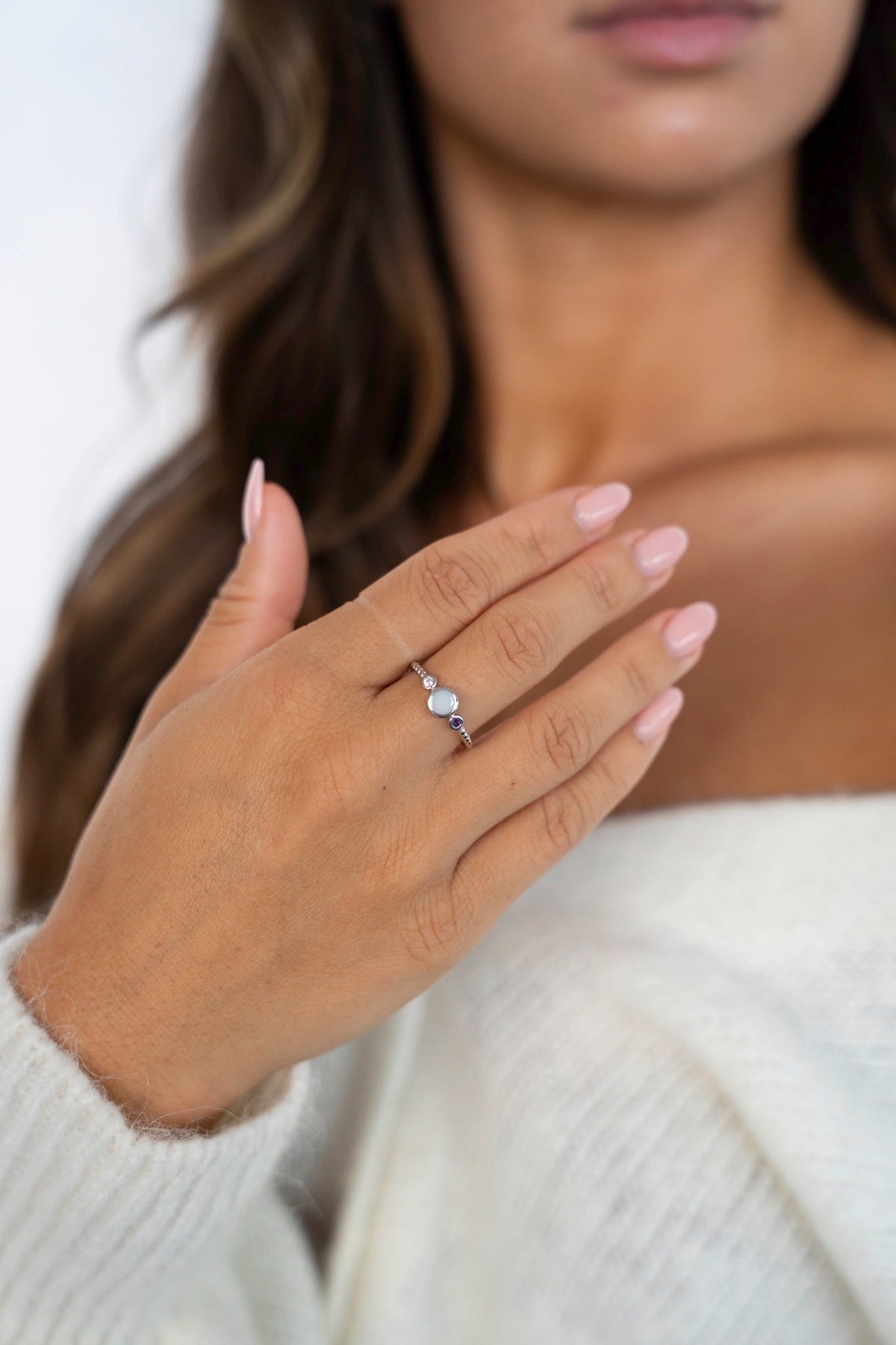 Hand wearing the Lot ring in white gold with breast milk and birthstones, against a white knit sweater.