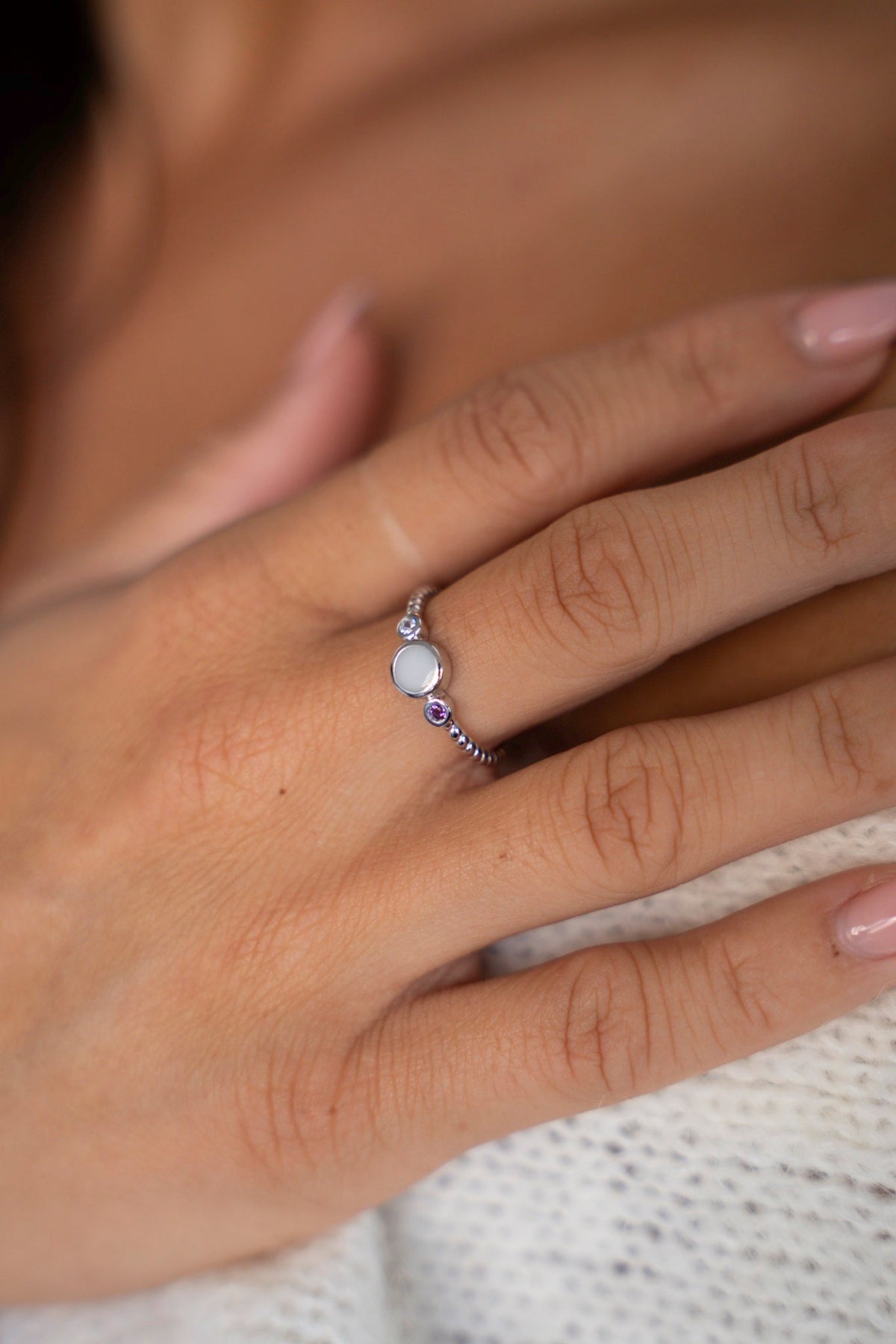 Close-up of the Lot ring in solid white gold with a twisted band, breast milk stone and purple birthstone, hand on the shoulder.