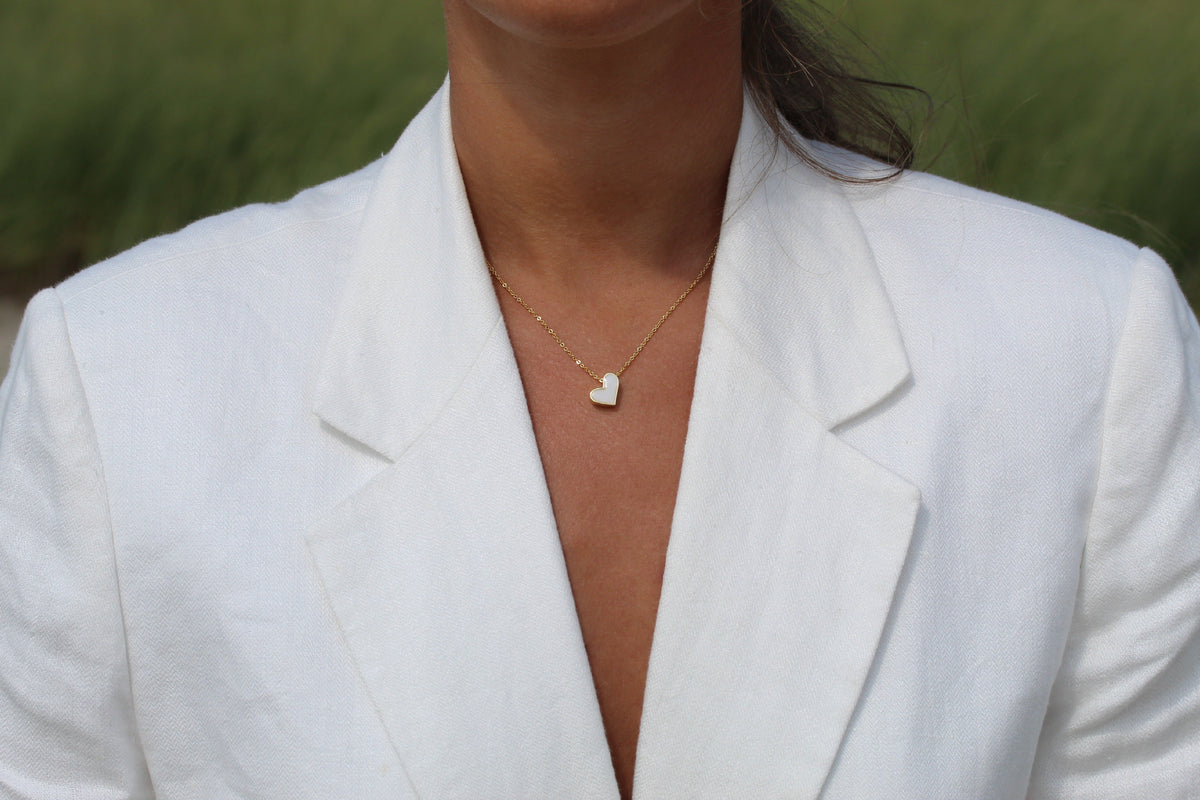 Louisa heart breast milk necklace in a gold color worn with a white linen blazer