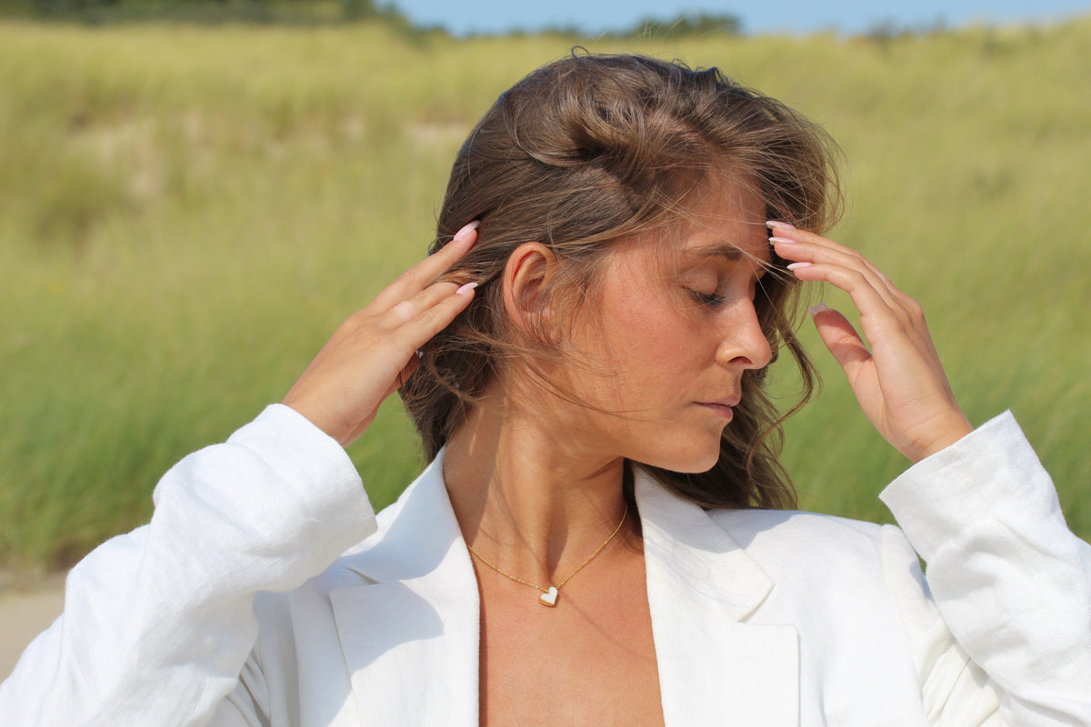 Woman holding her hair back, wearing a gold-colored Louisa heart necklace with breast milk