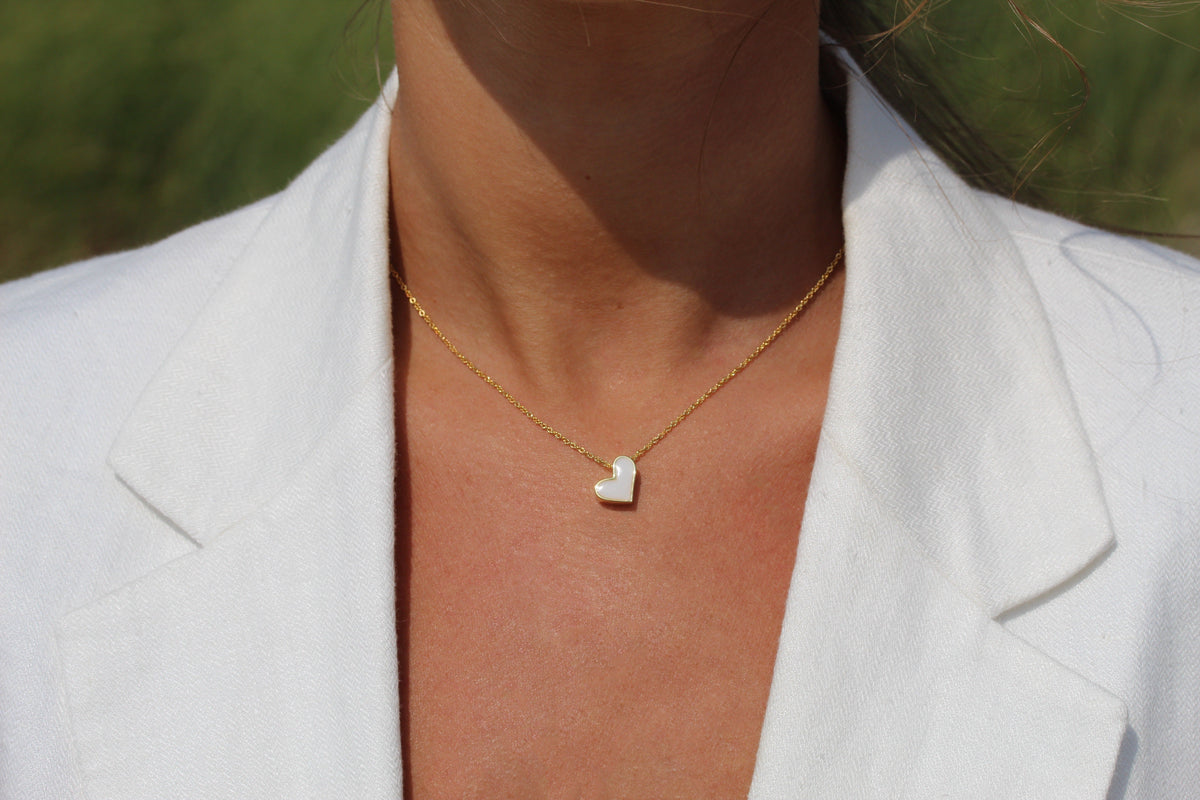 Close-up of a Louisa yellow gold heart breast milk necklace worn with a white blazer
