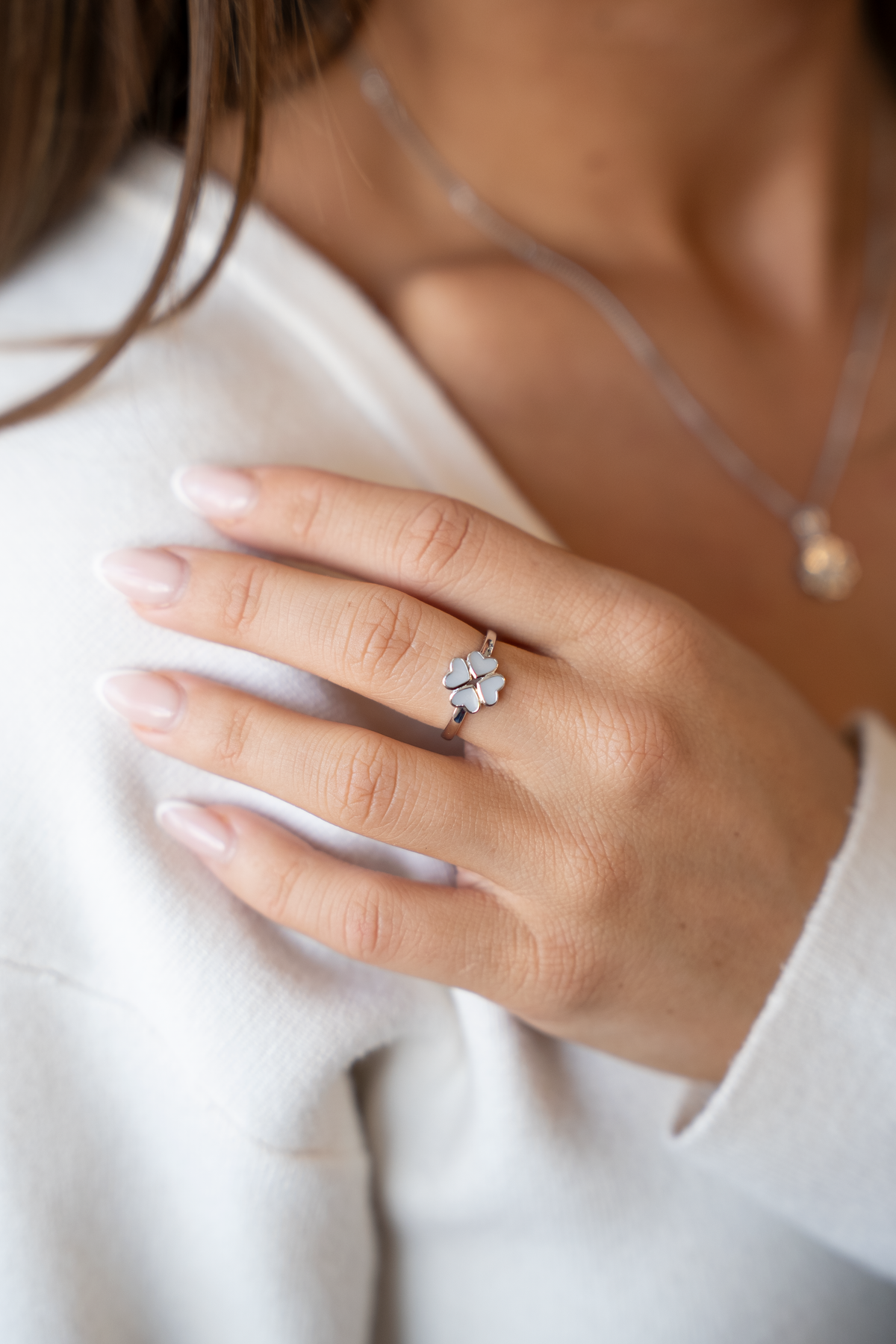 Silver Lucy clover breast milk ring on the finger, hand resting on the shoulder of a white sweater