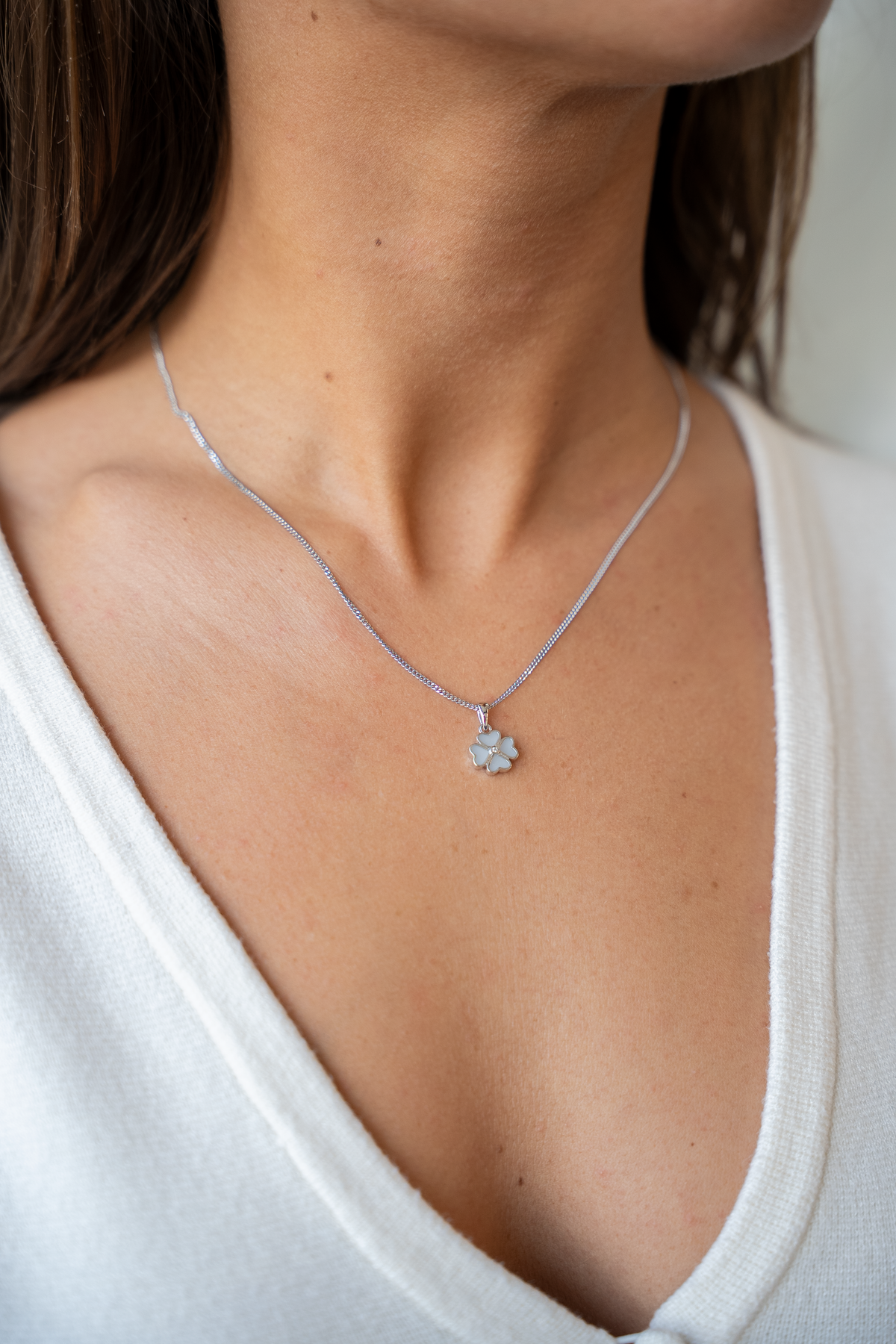 Close-up of the silver-tone Lucy breast milk clover pendant on a fine chain over a white cardigan