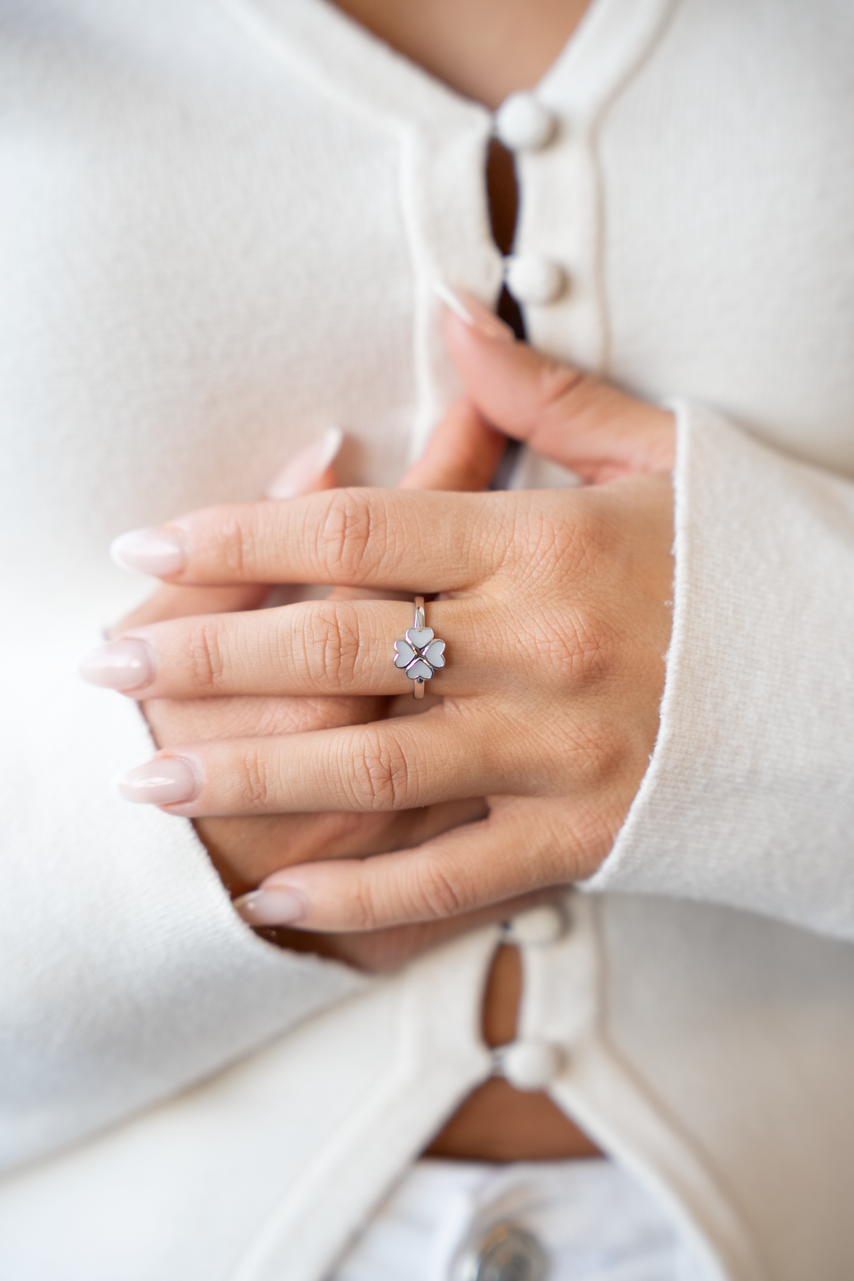 Lucy clover breast milk ring in white gold on the finger, hands folded against a white cardigan