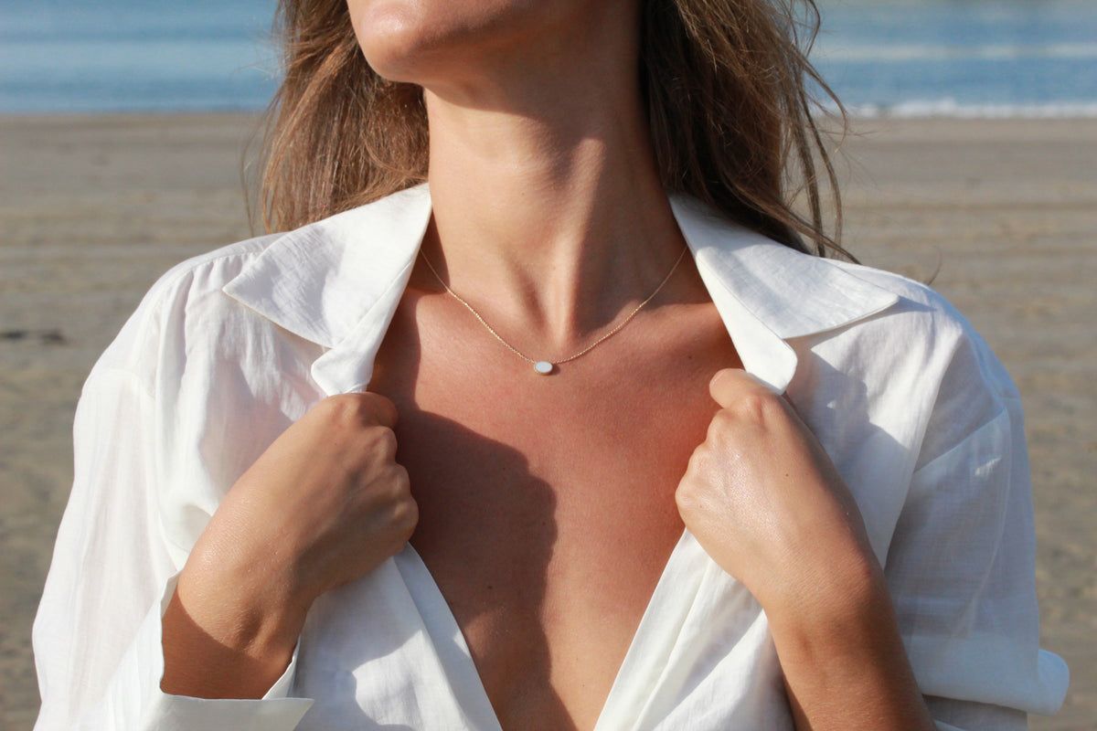 Luna oval breast milk pendant on a fine chain, worn with an open white shirt at the beach
