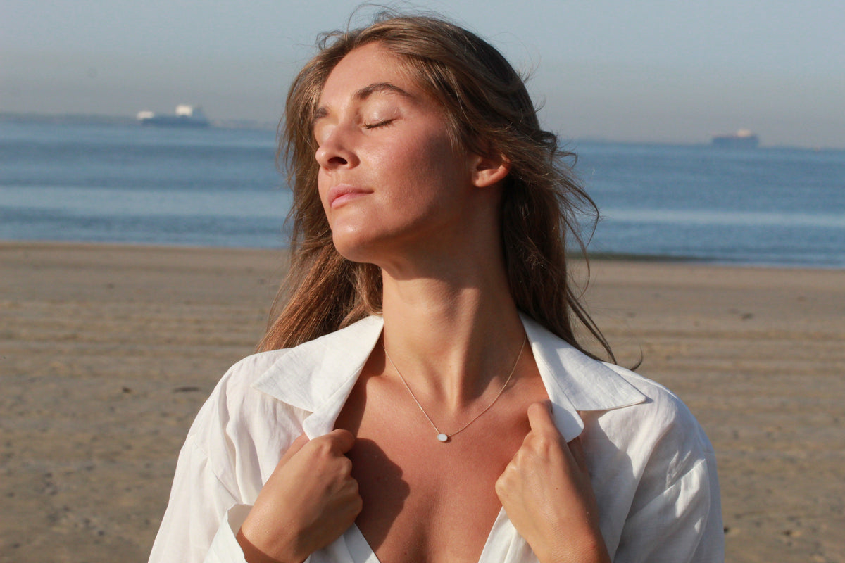 Woman enjoying the sun on a beach, wearing a Luna necklace with a small oval milk stone