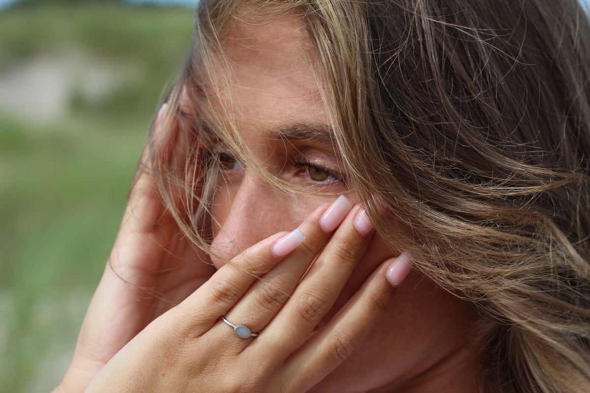 Close-up of the silver Luna breast milk ring on a hand by the face, windblown hair