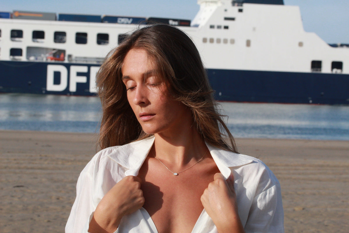 Woman in a white shirt by the water wearing a Luna necklace with an oval breast milk stone
