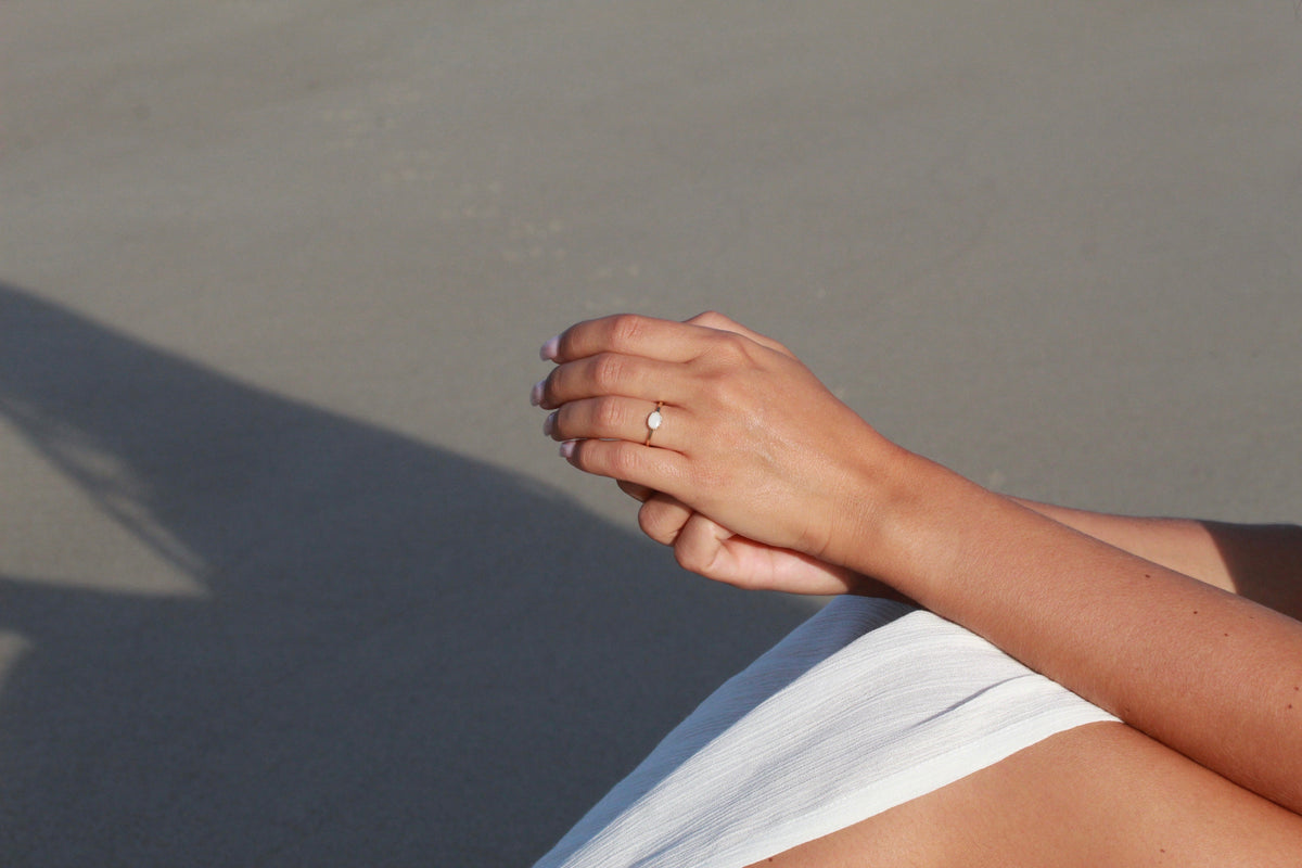 Luna breast milk ring worn on the finger, hands folded on a sunny beach