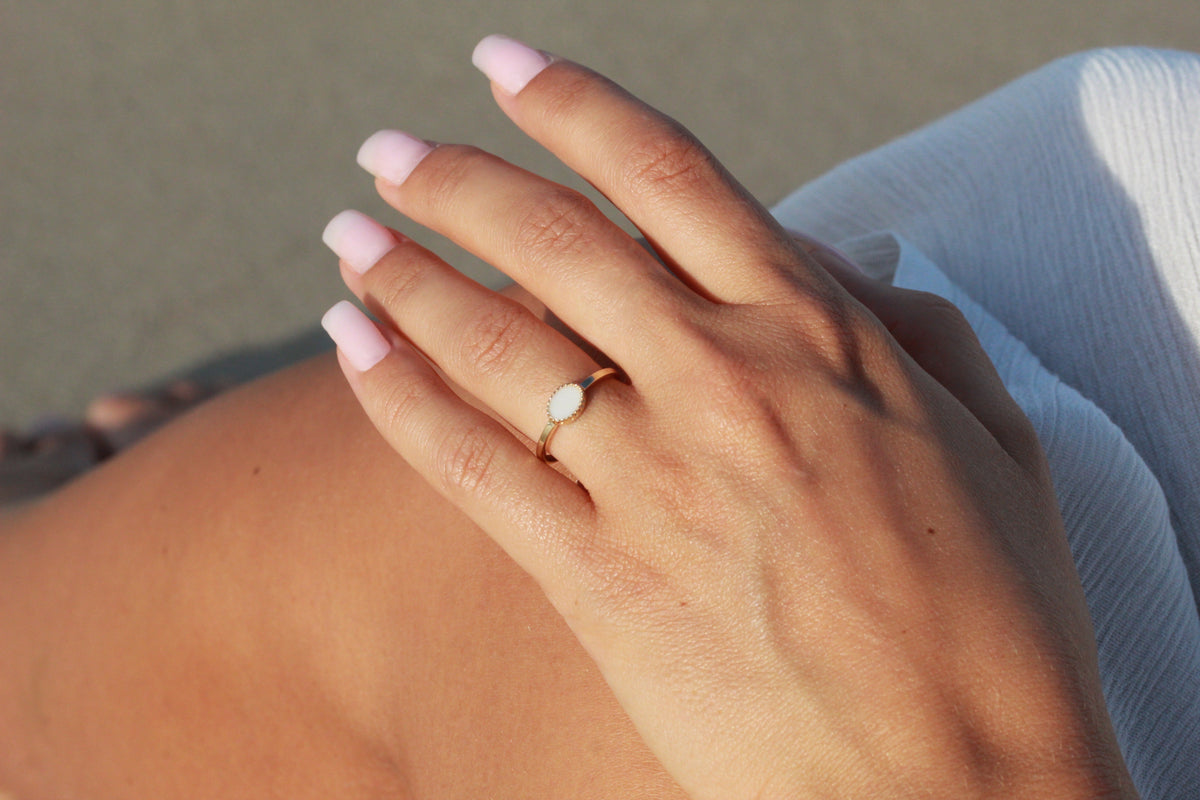 Luna breast milk ring in gold worn on the finger, hand resting on the hip in the sun
