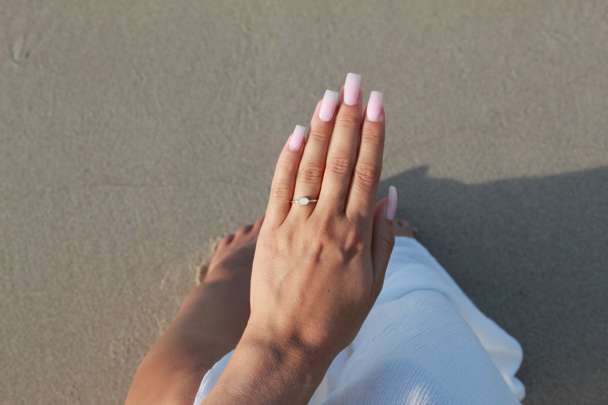 Luna breast milk ring worn on the finger, hand held up above the sand