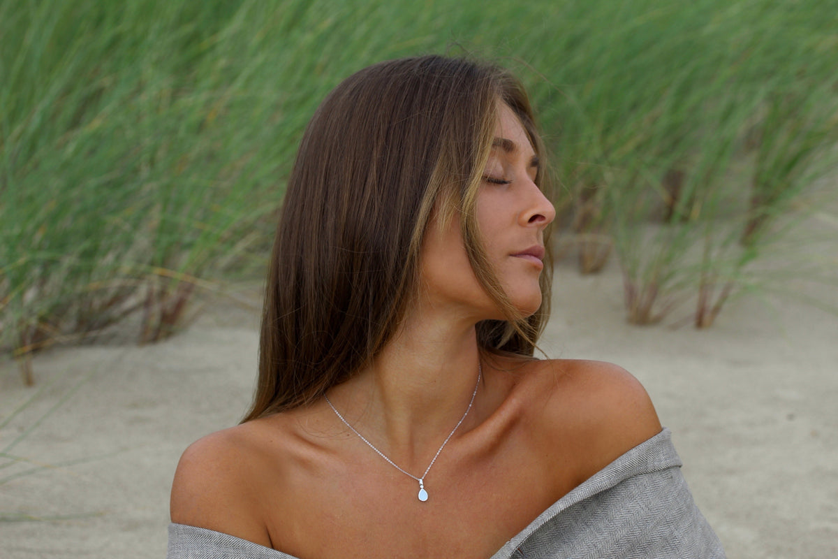 Woman in the dunes wearing the silver Magic Drop teardrop breast milk pendant on a fine chain