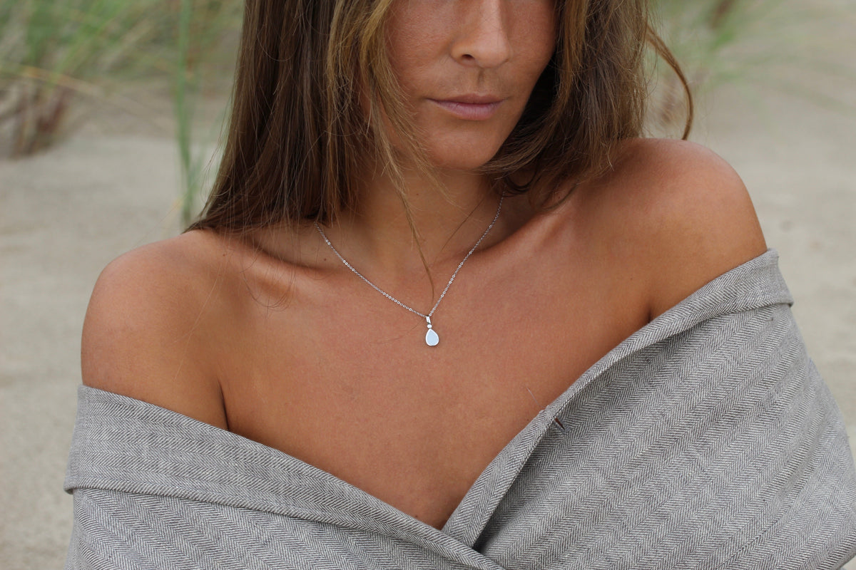 Close-up of the silver Magic Drop teardrop breast milk pendant worn on a fine chain with a gray wrap