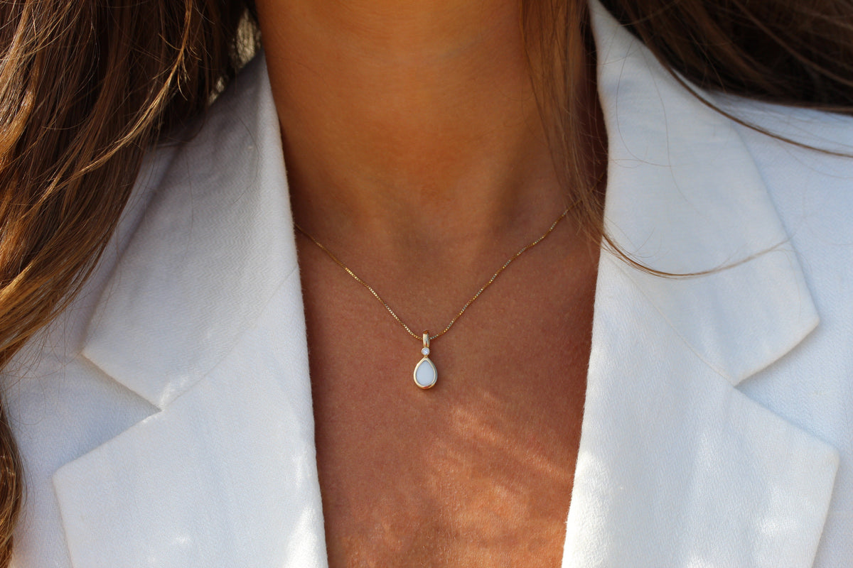 Woman in a white linen blazer wearing the Magic Drop teardrop breast milk pendant on a fine gold chain