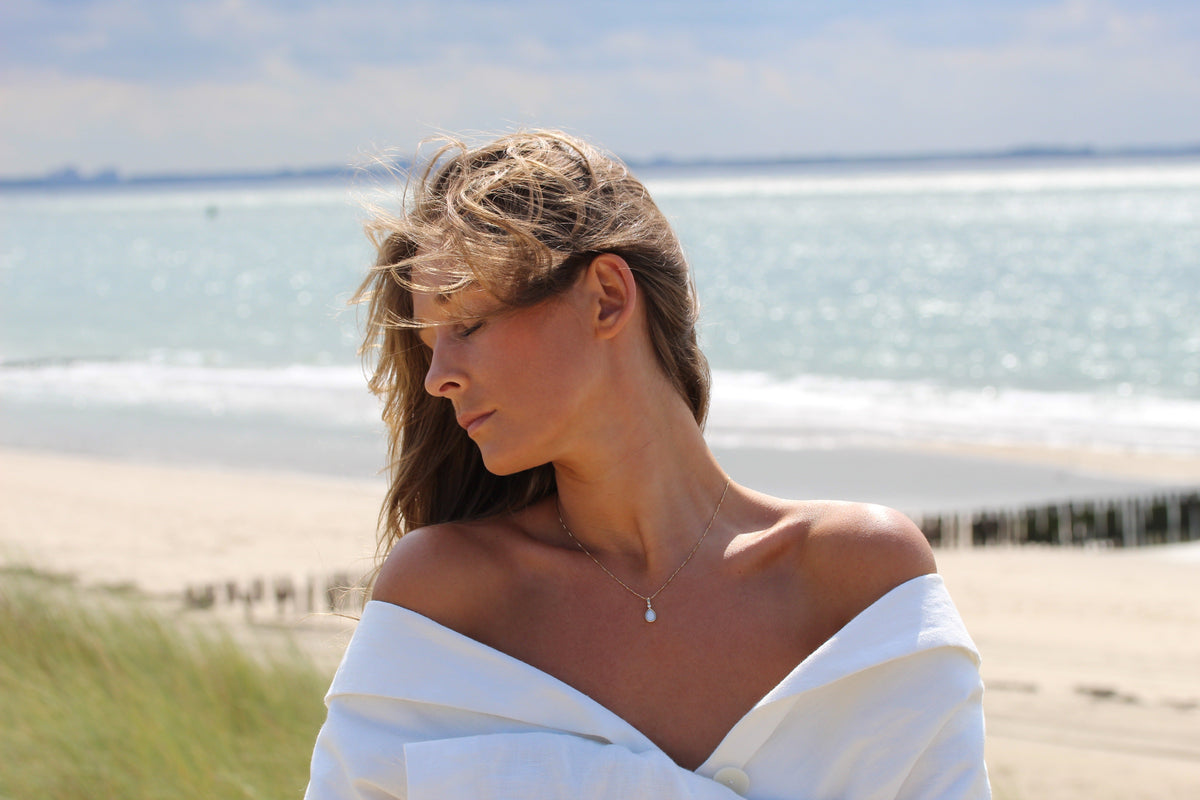 Woman on the beach wearing the Magic Drop teardrop breast milk pendant on a fine chain
