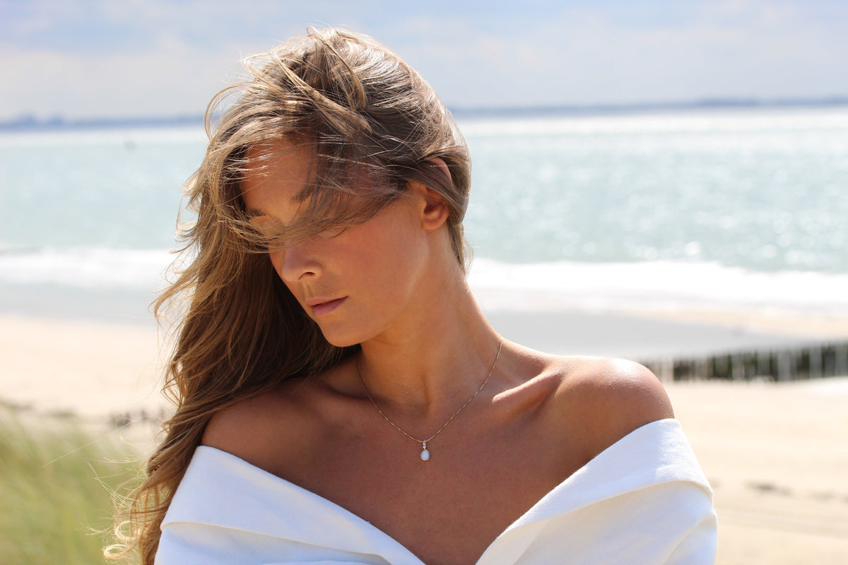 Woman with windswept hair by the sea wearing the small Magic Drop teardrop breast milk pendant